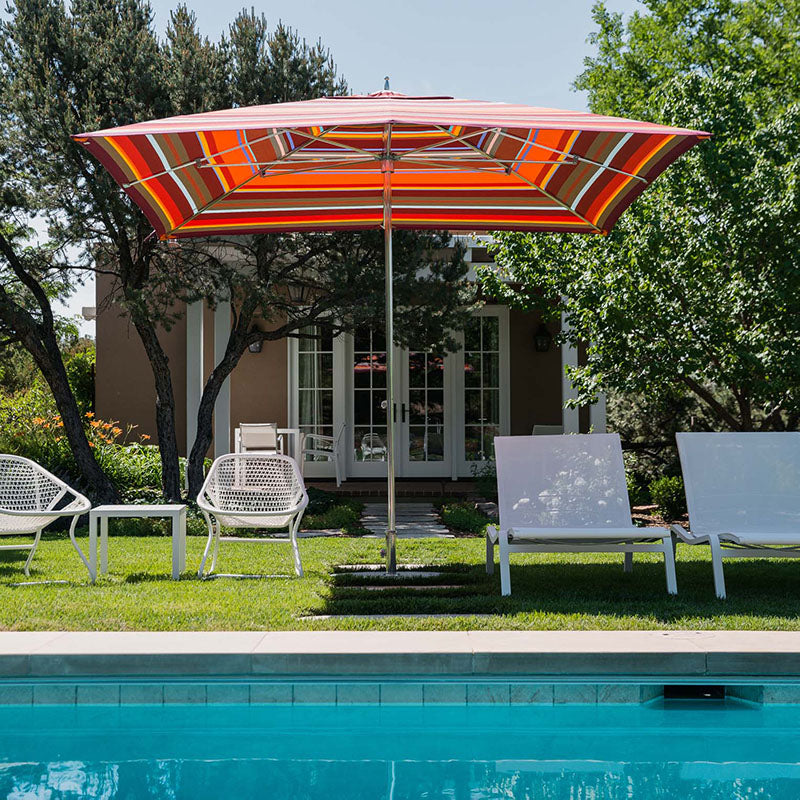 Tuuci umbrella with striped sunbrella canopy poolside with Fermob chaise lounges