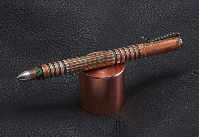 copper pen with green design placed on a cylinder copper