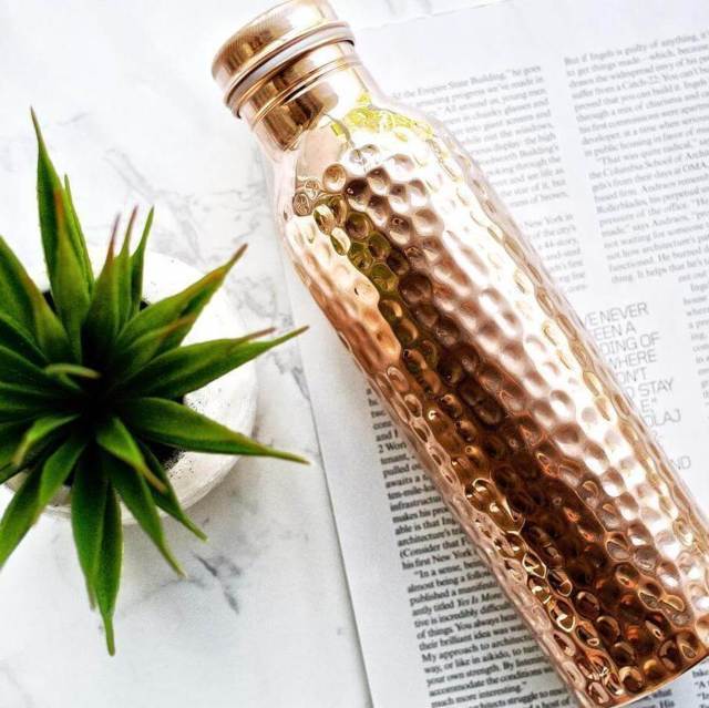 Copper H2O hammered copper water bottle placed on an open magazine