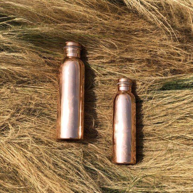 two Copper H2O smooth polished copper water bottles placed on hay