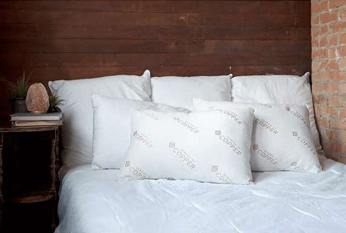 two Essence of Copper Pillow surrounded with larger white pillows placed on a single white duvet covered bed