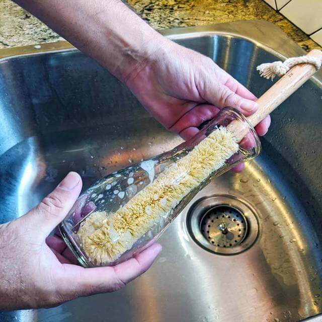 hand brushing the inside of a clear bottle using a natural bristle brush with wooden handle