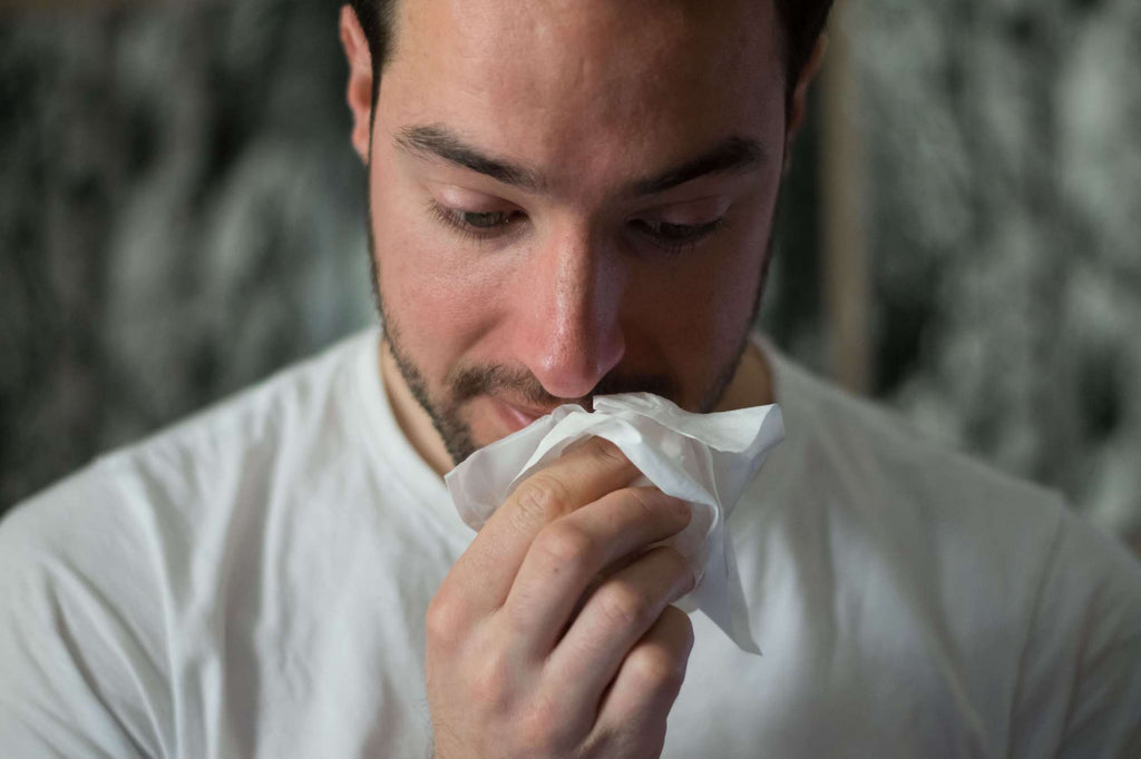 man wearing white shirt wiping tissue on his nose