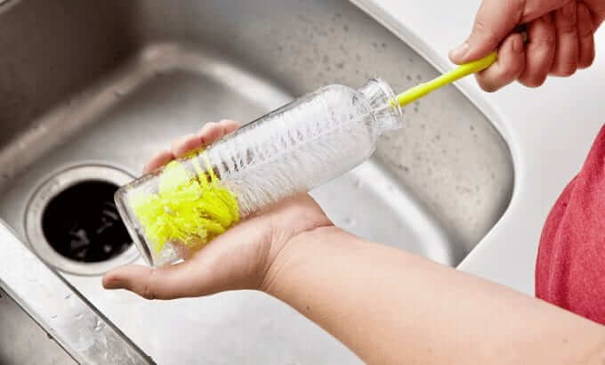 hand brushing the inside of a clear bottle using brush with yellow handle and bristle tips