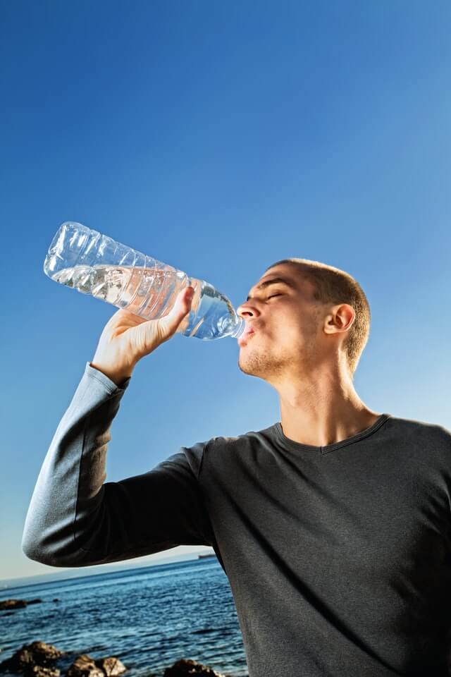 man wearing black shirt drinking water from plastic bottle