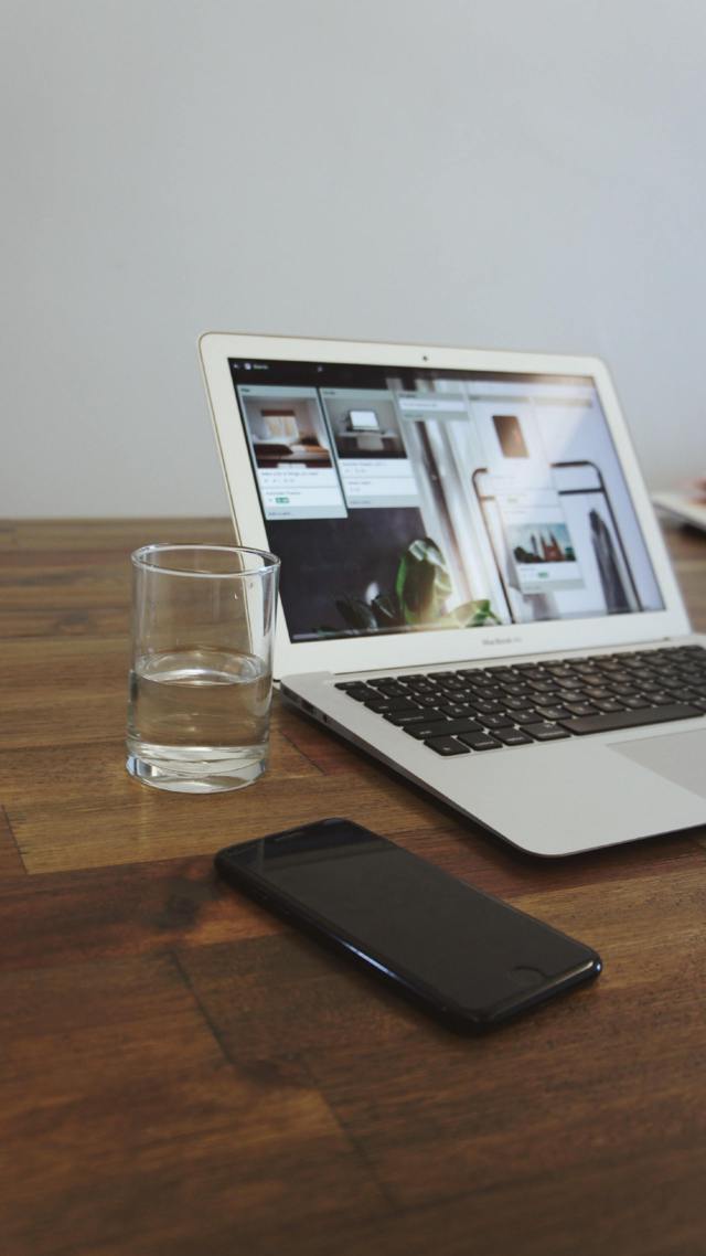 open laptop beside a glass of water placed on a wooden table