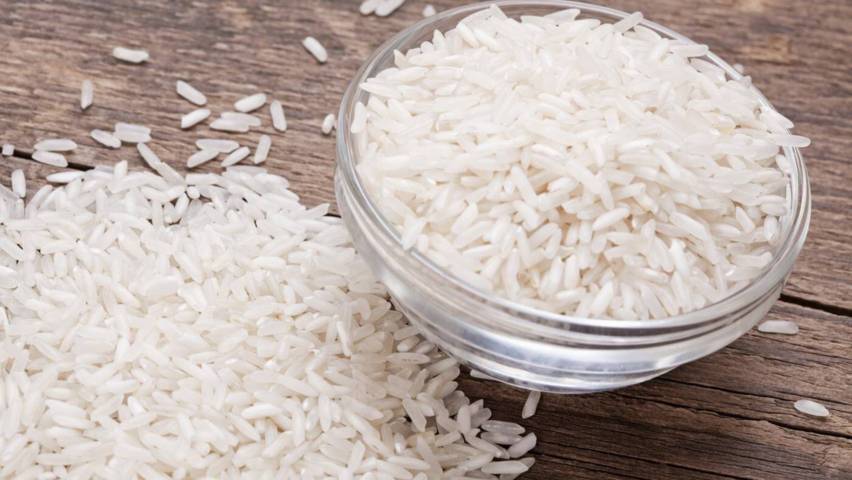 rice grains filled in a clear bowl some placed on wooden surface