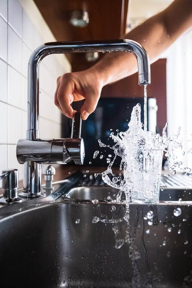 hand holding handle of faucet water gushing out