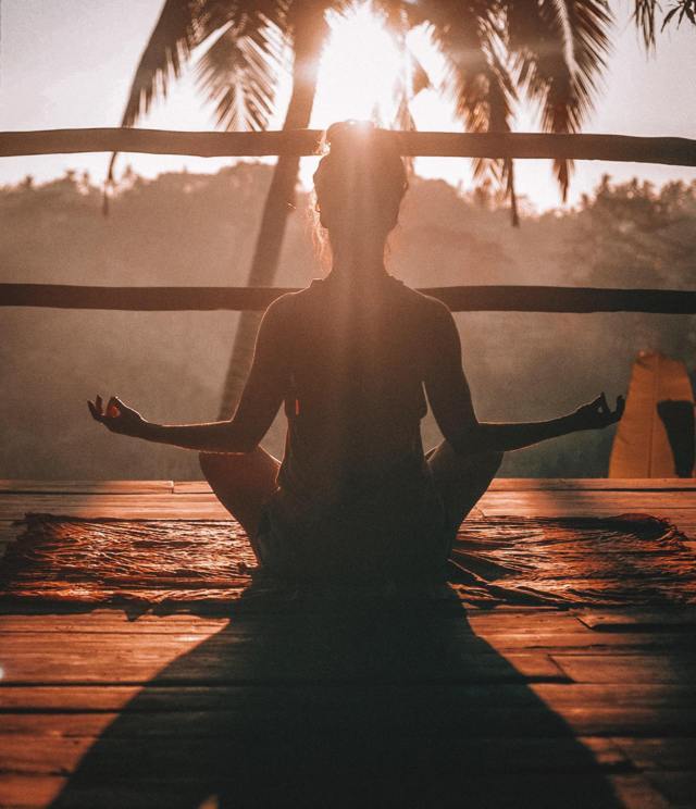 woman sitting in lotus position back to the camera facing the sun