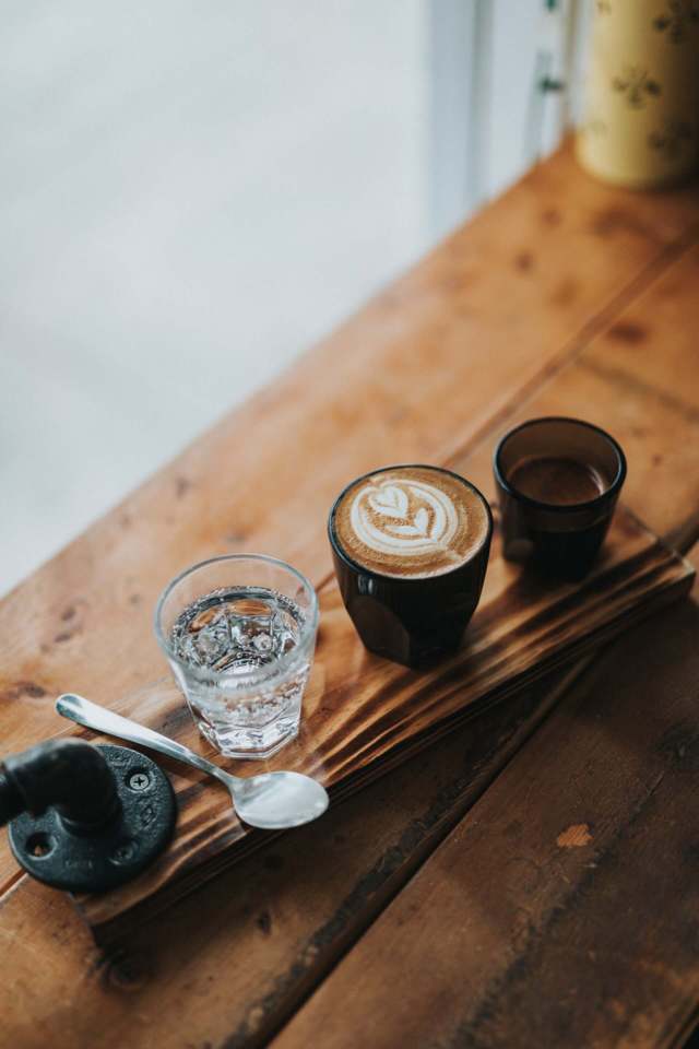 different cups containing water latte coffee spoon placed on a wooden surface