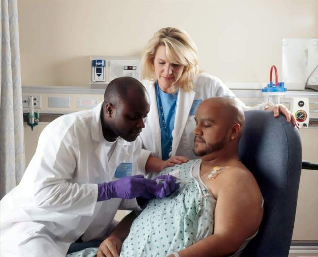 bald man being attended by two doctors in a hospital setting