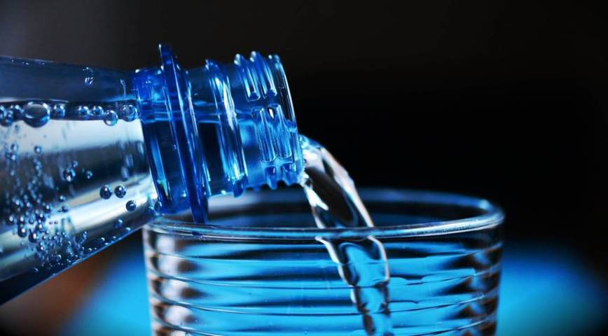 blue plastic disposable bottle pouring water into a cup