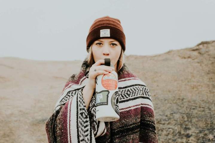 woman middle of the desert facing front sipping from a water bottle