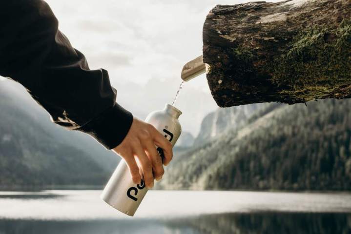 arm wearing dark jacker holding steel water bottle refilling water from a natural source