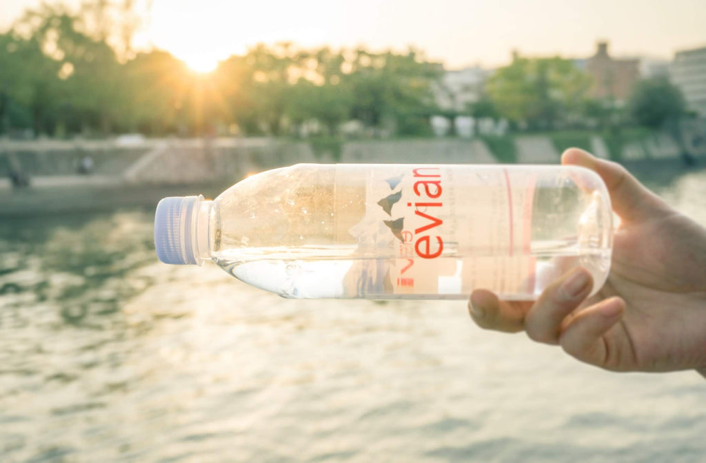 hand holding evian plastic disposable water bottle near a river