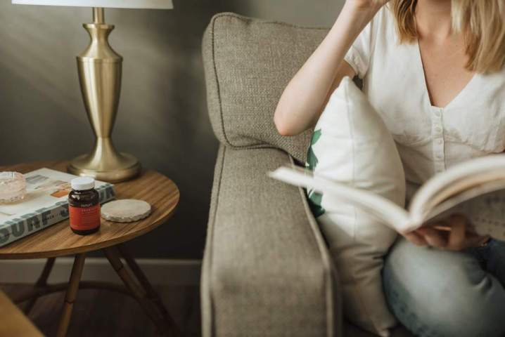 woman sitting on a sofa holding a book coffee table beside
