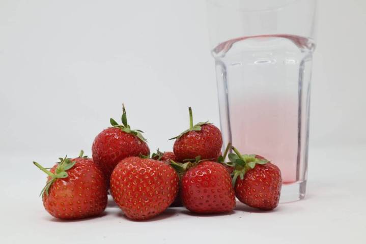 pile of strawberries glass of pink water beside white background