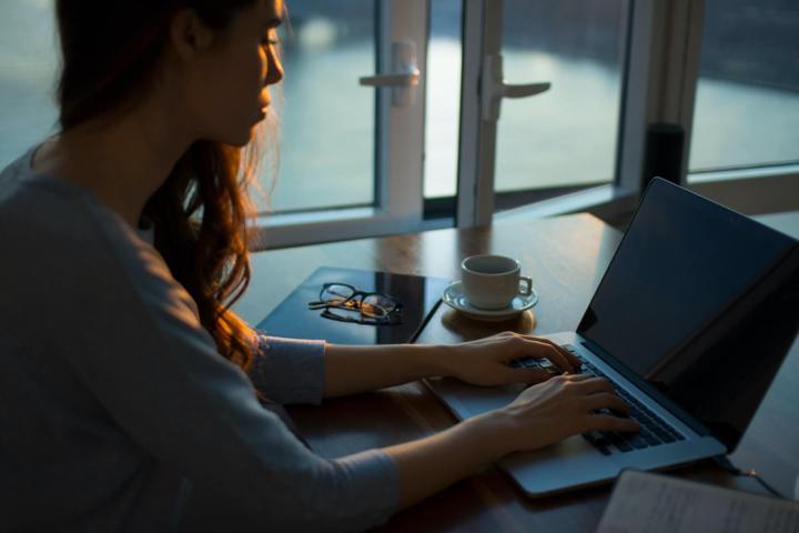 woman sitting beside table using laptop white mug and glasses on the surface