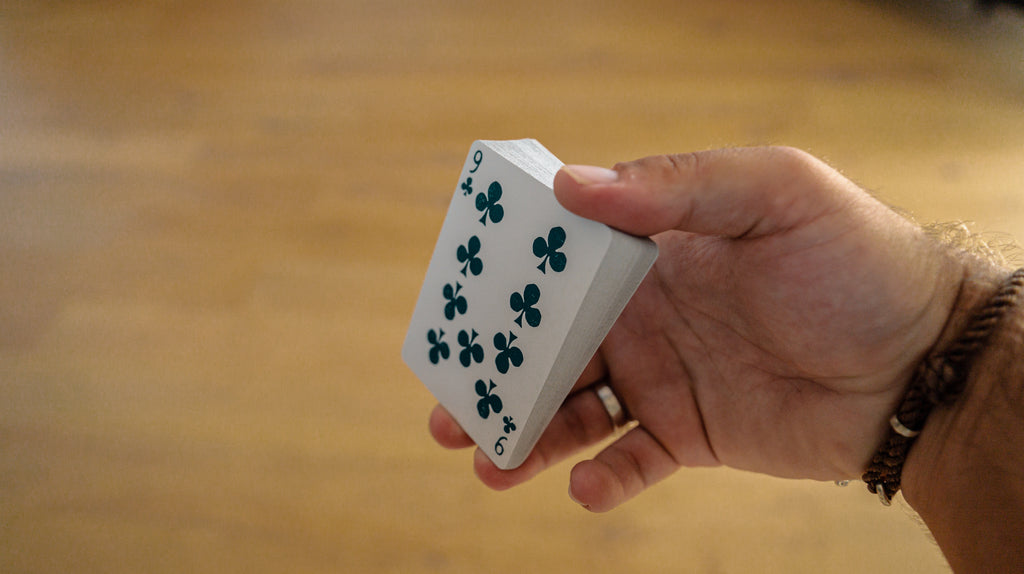 Person holding a deck of playing cards in Biddle grip. The nine of clubs is showing 