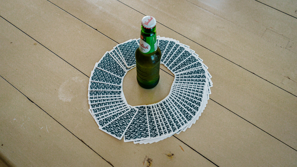 A deck of cards circled around a bottle of beer on a table ready to play king's cup the drinking game