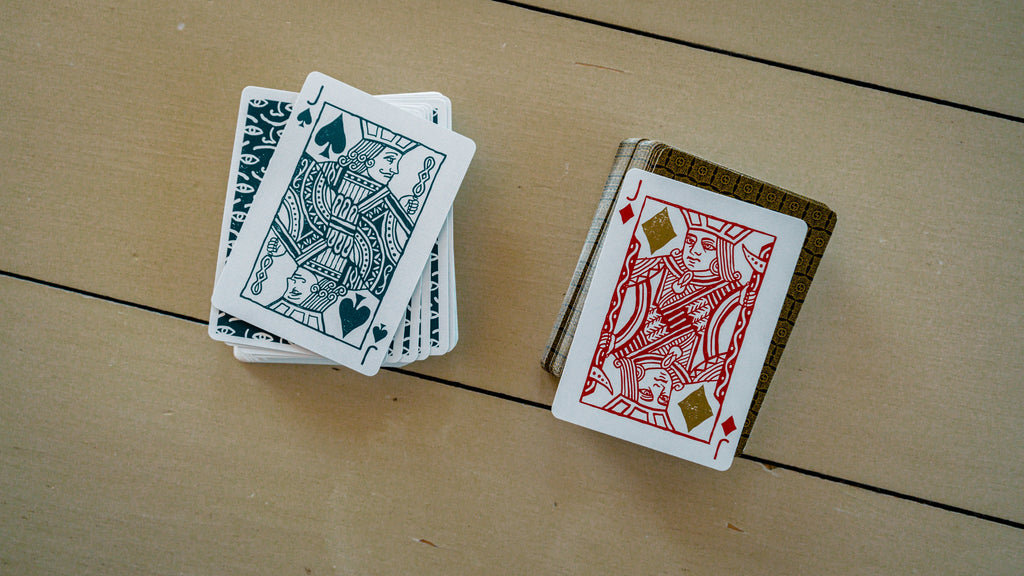Two decks of playing cards on a surface each with a jack card face up on the top of the decks