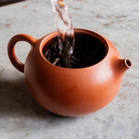 A photograph of hot water being poured into a clay teapot