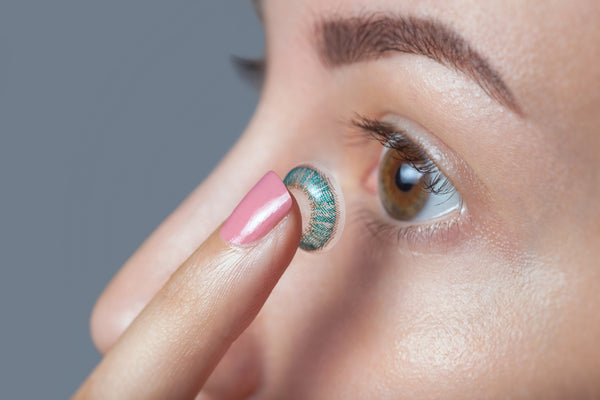 Woman holds a coloured contact lens on her finger.