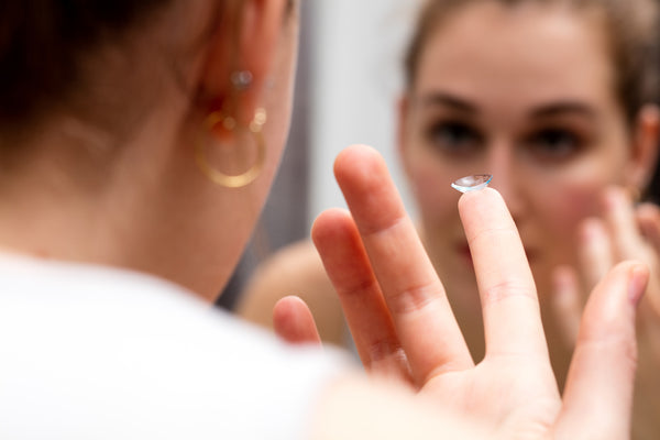 Young woman looking in mirror to change her contact lens.