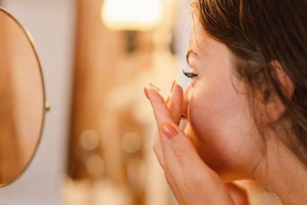 A girl facing a mirror applying contact lens.