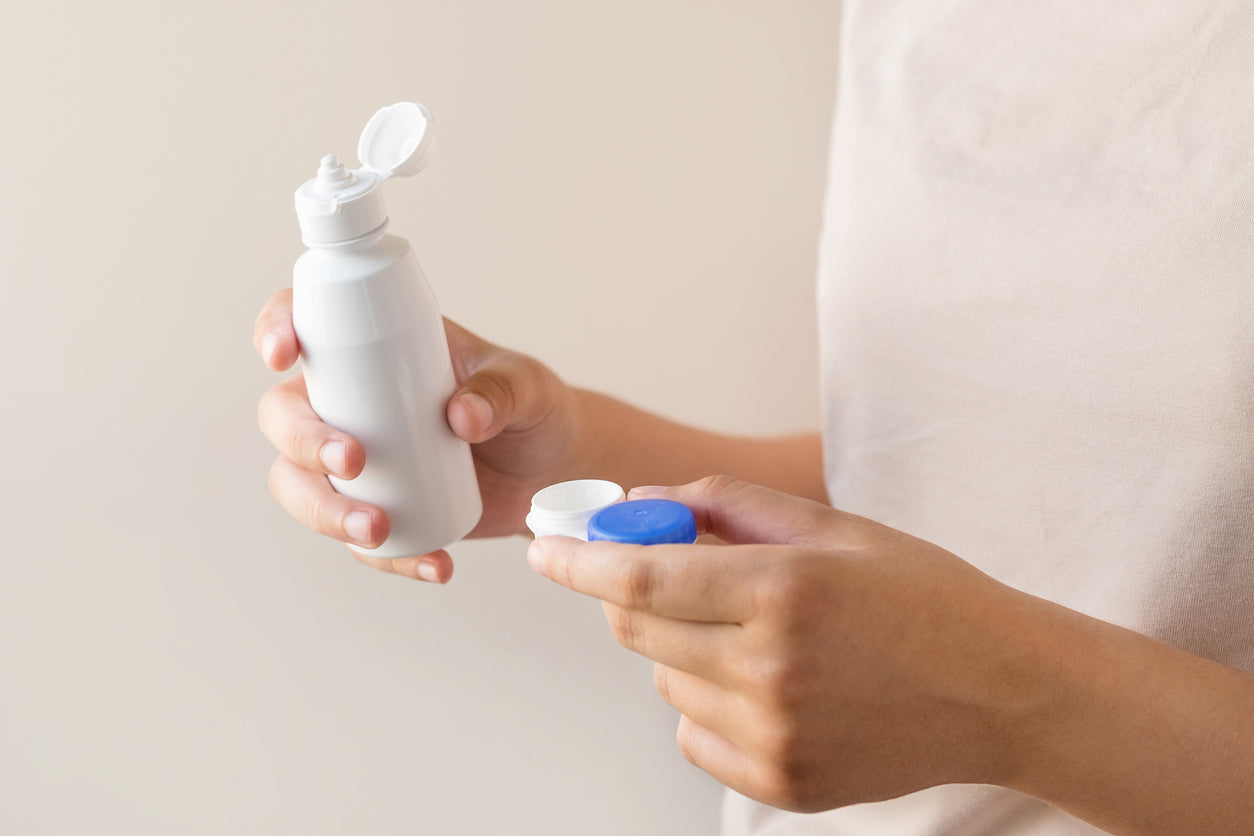 Women's hands with a solution and a container for contact lenses.