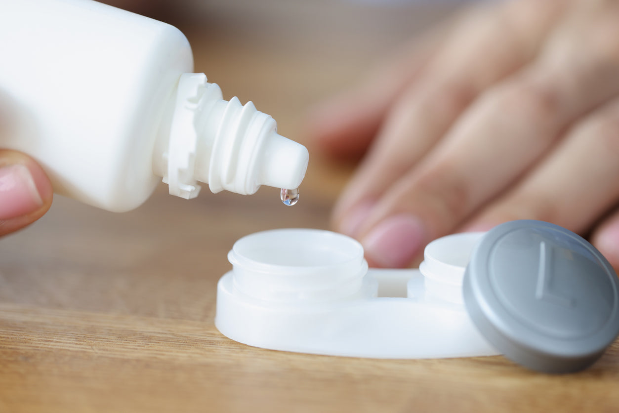 A hand pouring contact lens liquid into plastic container.