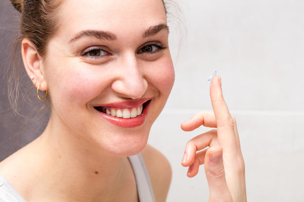 young woman smiling while holding a contact lens.