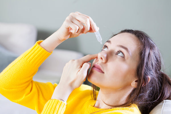 Closeup view of young woman applying eye drop.