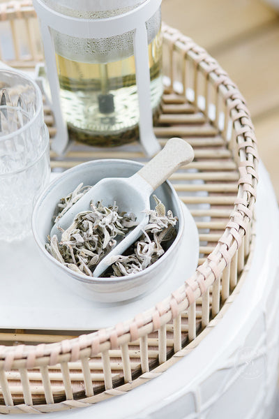 A bowl full of sage leaves with a scooper on a wicker platter.
