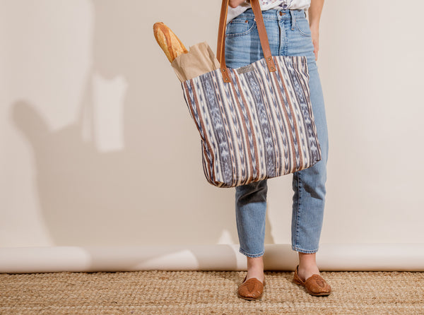 Young woman holding a farmer's market tote with bread in it.
