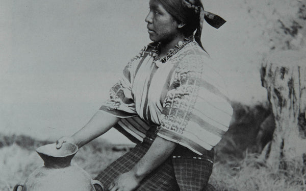 A black and white image of an indigenous woman in Guatemala on her knees, side profile, and holding a pot.