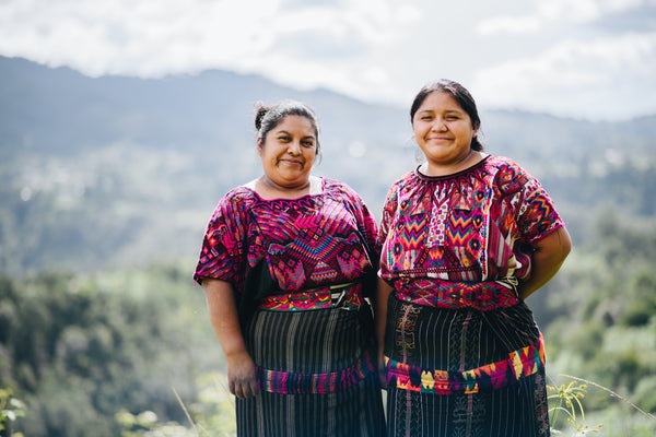 Two Guatemalan Women taking a picture in front of a landscape of trees and mountains