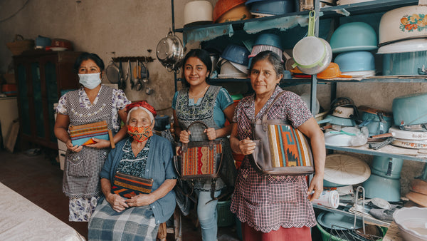 Four Guatemalan women taking a picture holding the bags with the textiles they handmade on them for Nena & Co.