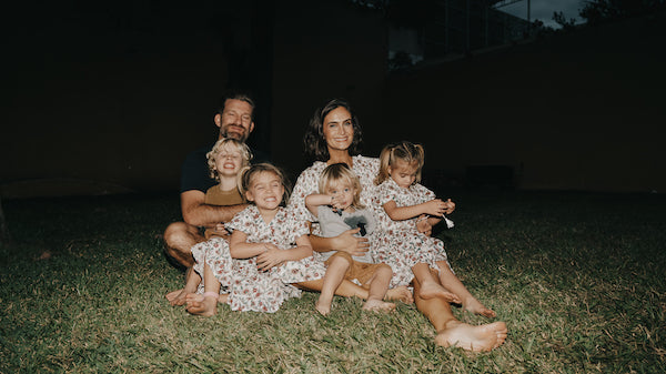 Ali and Jeremy Hynek sitting outside on the grass in Mexico with their kids on their laps for a photo opportunity.