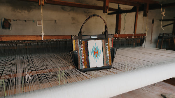 A beautiful Nena & Co. handbag from the Mexico Collection sitting on top of a footloom used to create textiles.