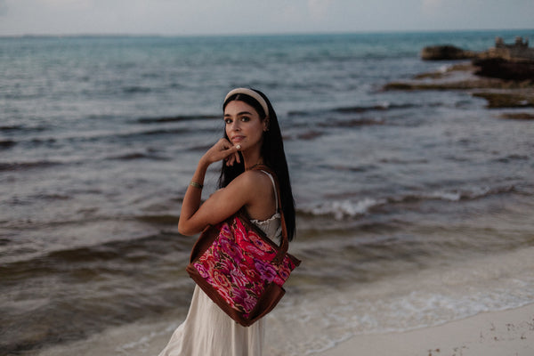 Young woman in a dress holding a Nena & Co. bag made of upcycled huipils on her shoulder on the beach.