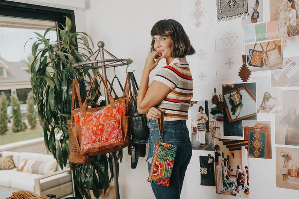 Woman modeling in front of some bags looking behind her shoulder at the camera and some mood boards behind her.
