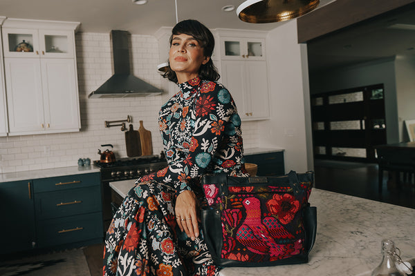 Ali Hynek sitting on her kitchen island looking at the camera with a handbag to her side