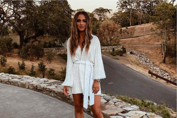 woman in a white romper and long hair modeling outside in nature but in front of a road.