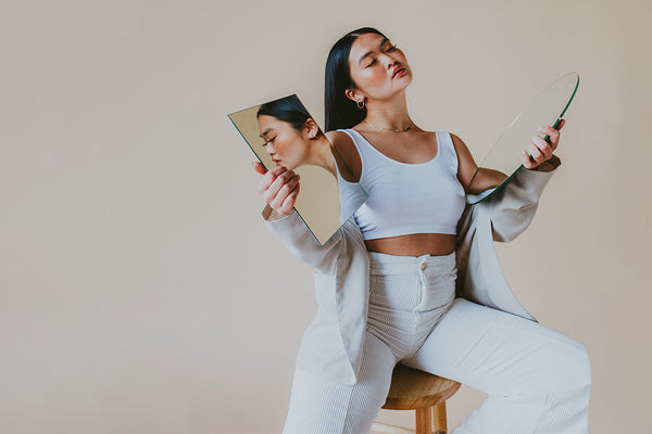 Asian young woman modeling mirrors in front of a backdrop sitting on a stool.