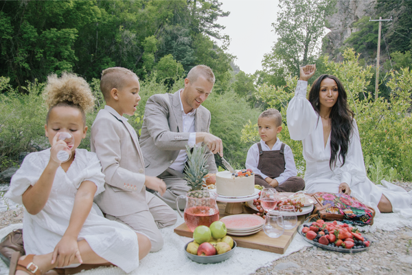 Biracial couple with there three kids having a picnic by a river celebrating Juneteenth with her hand in the air.