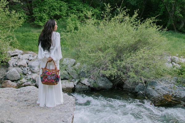 black woman standing in front of a river look down while holding a handbag behind her back.