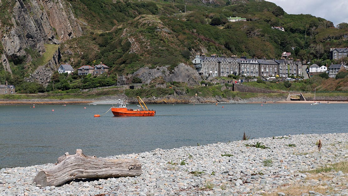 An orange fishing boat moored in the Mawddach Estuary with Wales in the background