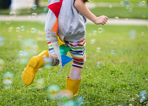 kid with rainbow dinosur tail running in bubbles with rubber boots