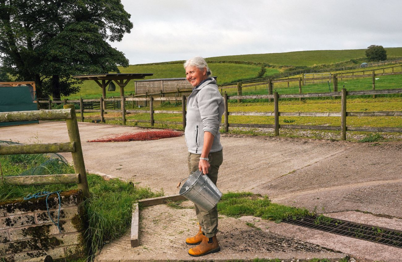 Deborah Griffin holding a metal bucket on the farm to feed the sheep